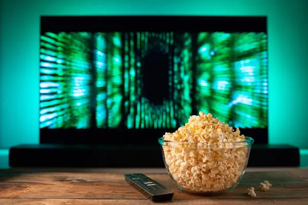 Bowl of popcorn and remote control in front of a TV screen displaying a futuristic green digital design