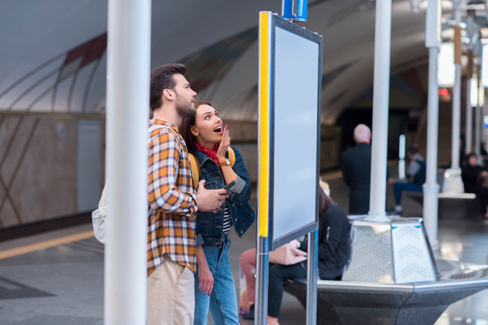 Young couple in a subway station looking at an advertising display, engaging with digital media content in a public space.